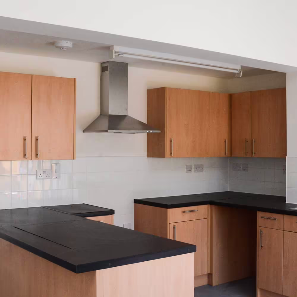 A newly installed, modern kitchen in a converted residential property, featuring light wood cabinets, black countertops, and a stainless steel cooker hood.