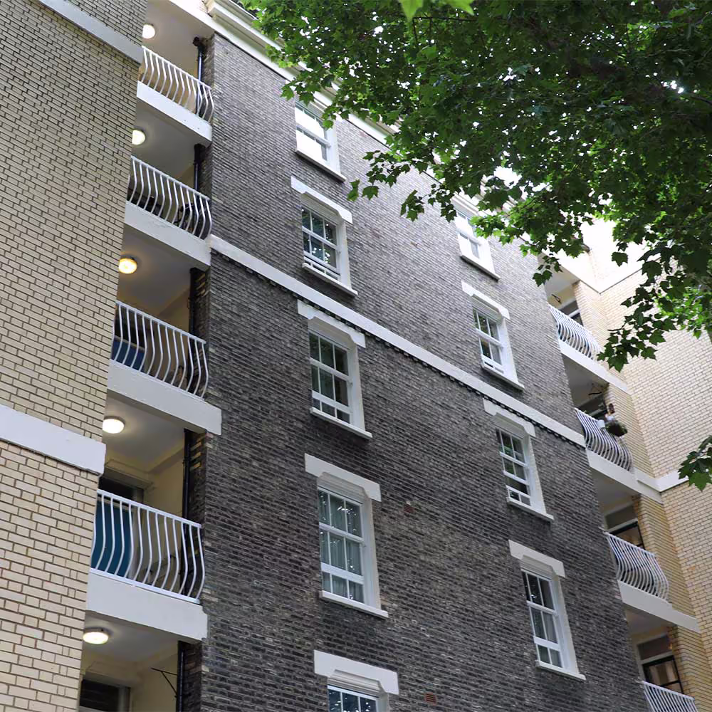 The repaired facade of a London apartment block, showing the clean brickwork, restored white sash windows, and modern balconies following residential repair works.