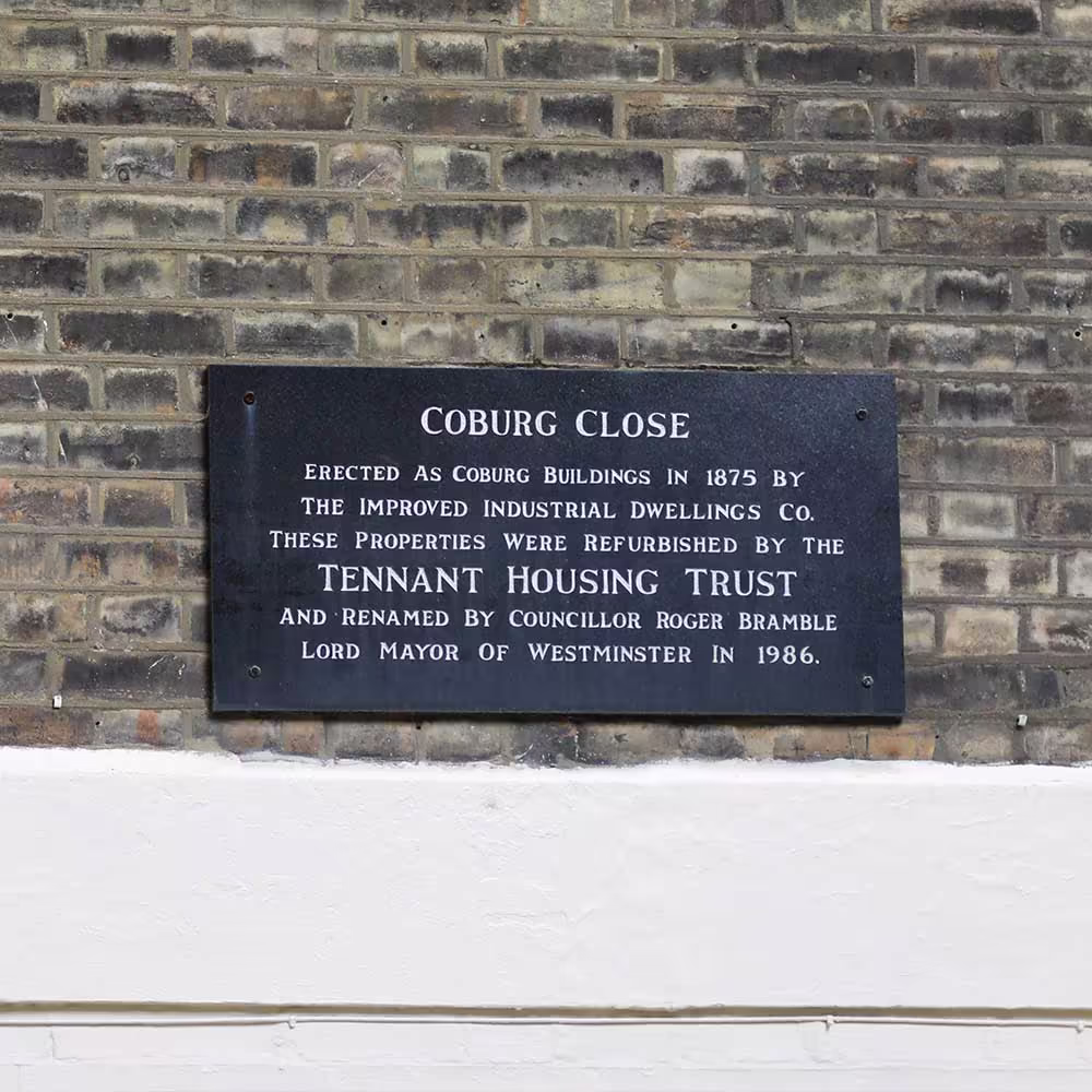 The historic plaque on Coburg Close in Westminster, detailing its history and refurbishment by the Tennant Housing Trust, a site of residential repairs.