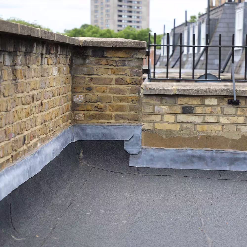 A repaired flat roof on a residential building, showing the new lead flashing expertly installed against the brick parapet wall.