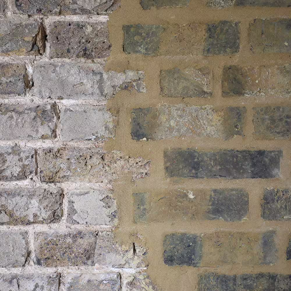 A close-up, split-view of an old brick wall, demonstrating restoration work. The left side shows rough, weathered brick and mortar, while the right side shows cleaned brick with new, tan-colored pointing/mortaring.