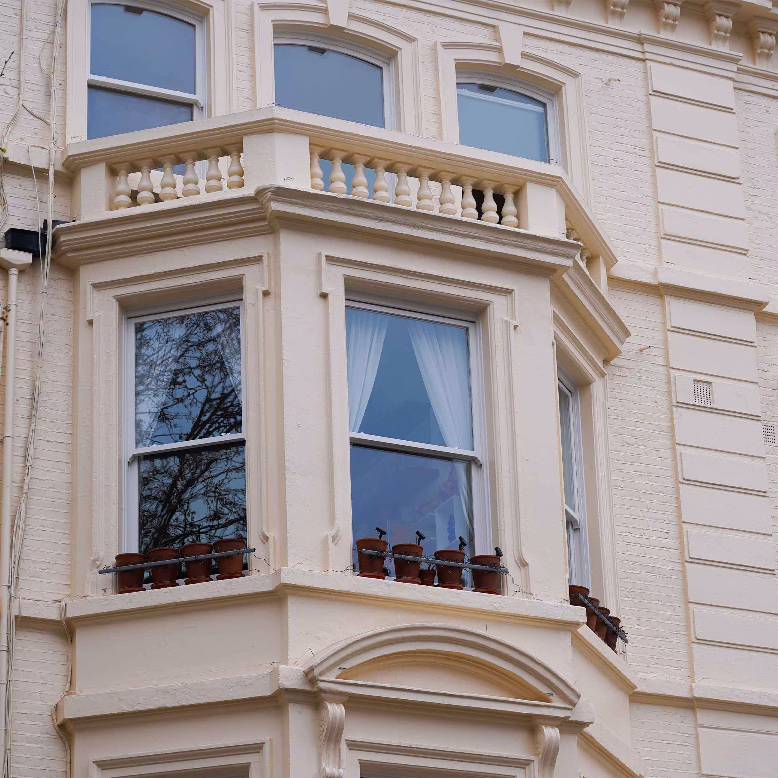 A close-up of a first-floor bay window on the refurbished townhouse, showing the ornate balustrade balcony, fresh paintwork, and the restored white sash windows.