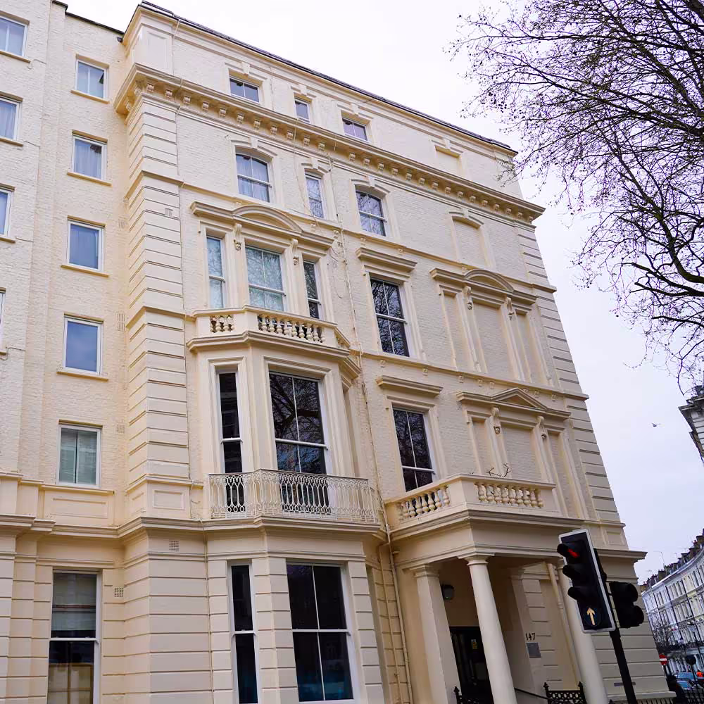 A tall, imposing view of a recently refurbished London townhouse facade in pale cream, emphasizing the symmetry, detailed cornices, window casings, and bay windows after extensive roof and window repair work.