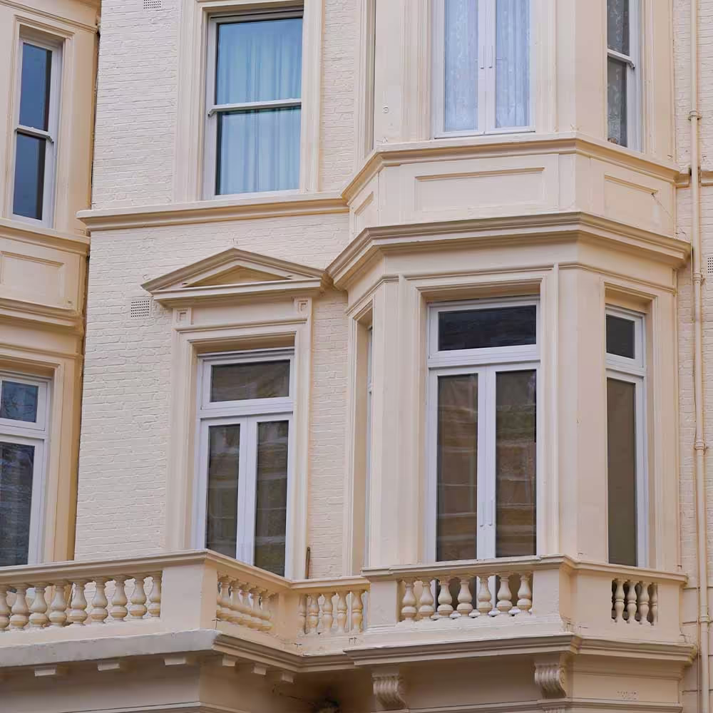 A close-up of a second-floor window and balcony area on the refurbished townhouse, showing the white frames of the new sash windows and the detailed plasterwork of the facade.