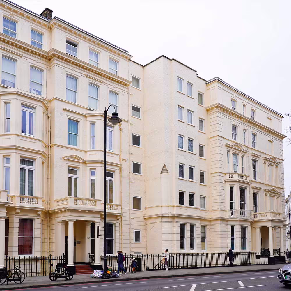 A street-level, wide view of a continuous row of refurbished luxury townhouses painted in pale cream. The image showcases the completed exterior restoration and window repairs on the historic properties.