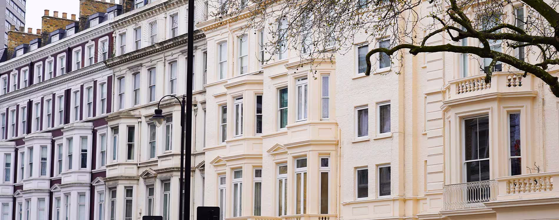 A row of newly refurbished, elegant Victorian/Georgian terraced townhouses in London. The building in the foreground is painted pale yellow/cream, highlighting the new rooflines and white windows after repair work.