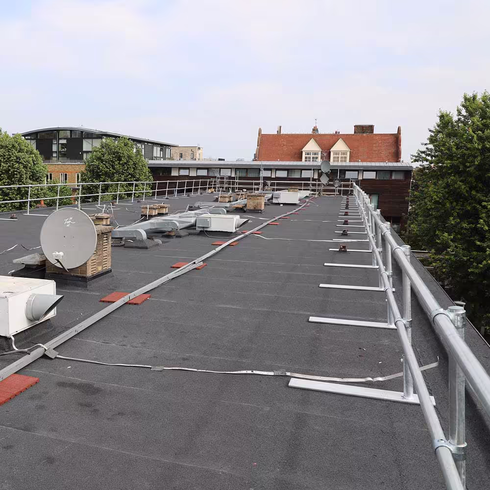 A perspective shot showing the expanse of the renewed dark grey flat roof. It includes newly installed safety guardrails and bases, along with existing mechanical equipment like satellite dishes and HVAC components.