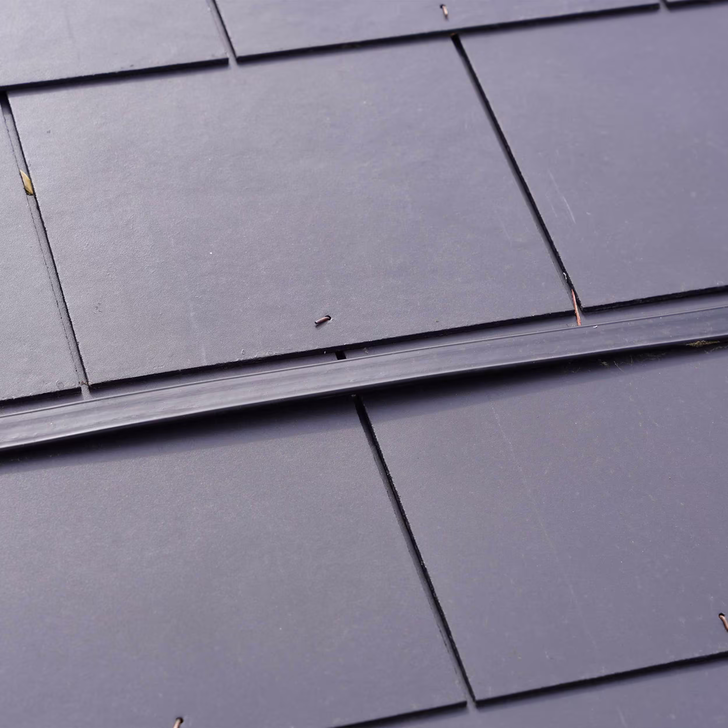 A detailed close-up of the seam between four of the new dark grey slate roof tiles, showing the clean finish and the linear batten or joint cover in between, emphasizing the quality of the new roofing installation.