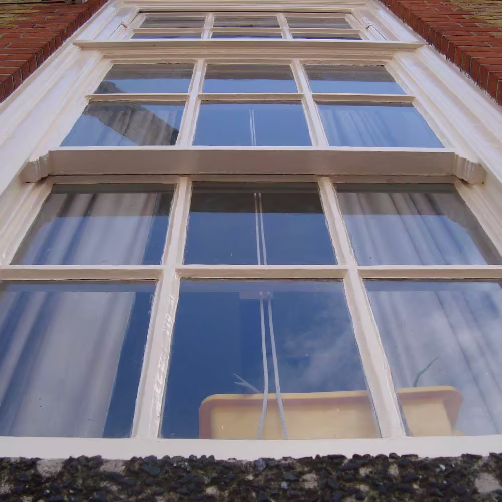 A low-angle close-up of a freshly painted, white-framed sash window on the school building, emphasizing the detailed glazing bars and the quality of the window renovation.