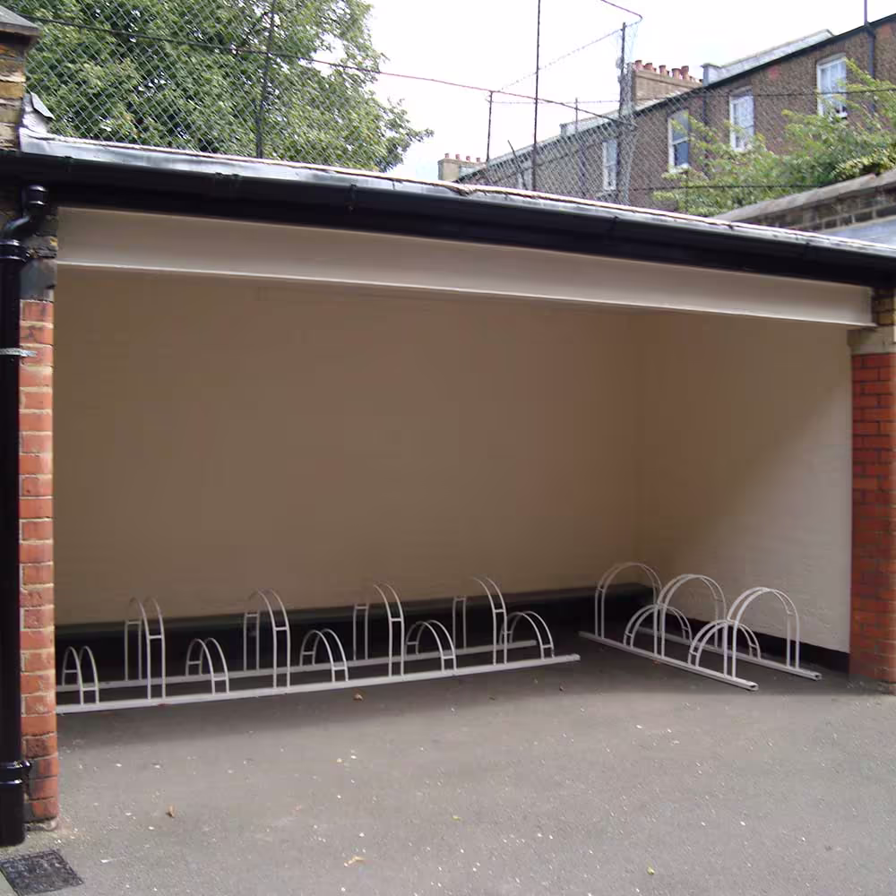 A newly constructed or renovated covered outdoor bike storage area in the school playground, featuring a clean, painted interior and white metal bike racks.