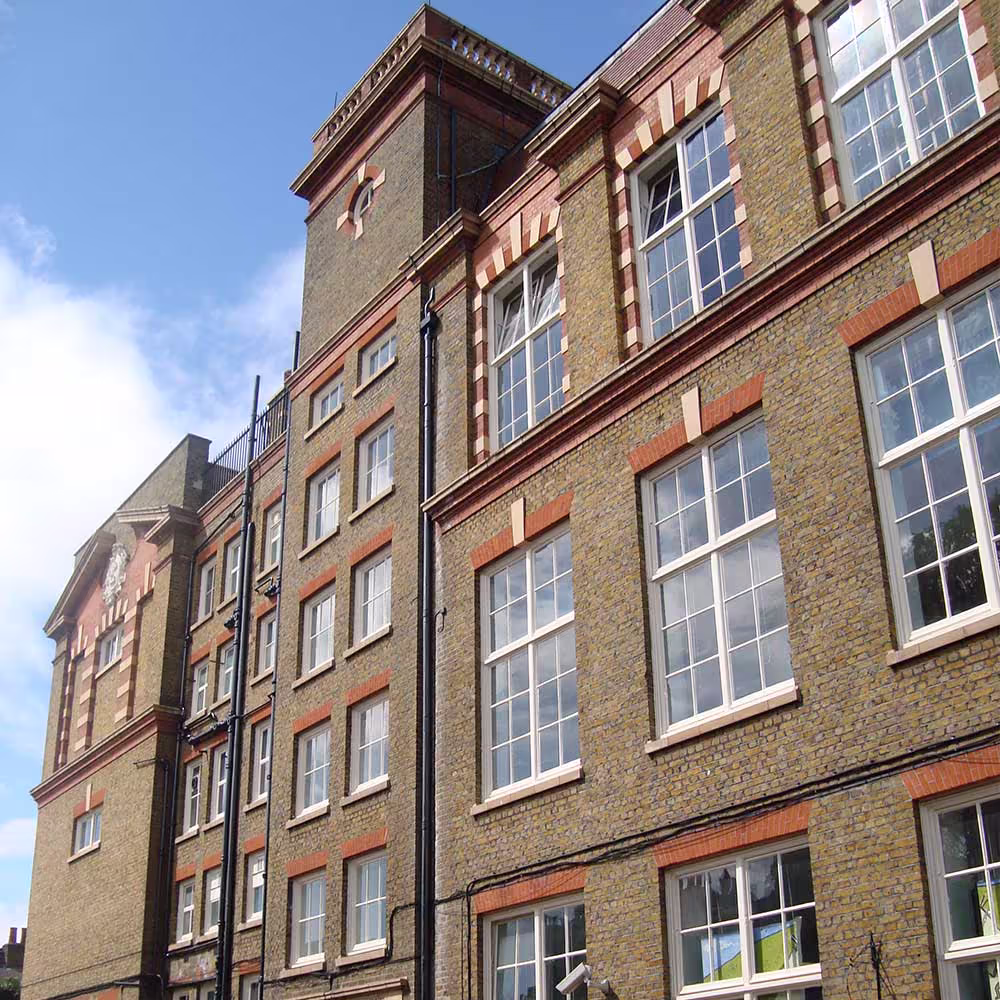 An upward-angled close-up of the historical school building facade, highlighting the multiple stories, tall window arches with red brick trim, and the decorative top section of a tower, indicating a major school renovation project.