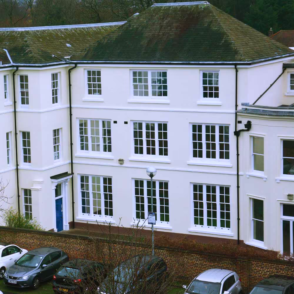 The exterior of the renovated educational building where the lab is located, featuring a smooth, pale cream facade with large, multi-paned white windows and a slate roof, showcasing the overall building refurbishment.