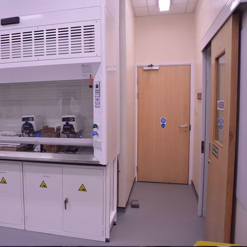 A safety-focused shot inside the refurbished lab, showing a fume cupboard next to a fire-rated wooden door and an adjacent viewing window door, ensuring safe and easy access to the laboratory space.