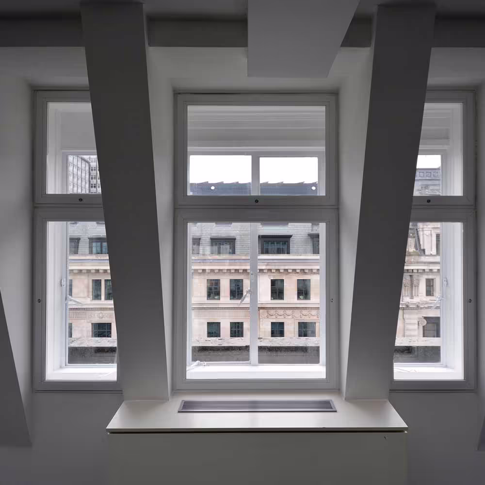 A symmetrical view of three newly installed white-framed windows set into deep, angled recesses, with a cityscape of traditional buildings visible outside, demonstrating the architectural window features of the renovated office.