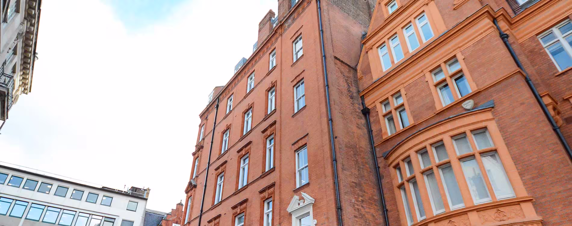 An upward-angled view of the facades of two ornate, red brick Victorian buildings. The building on the right features terracotta or orange-painted stucco around large bay windows, highlighting the historic property renovation.
