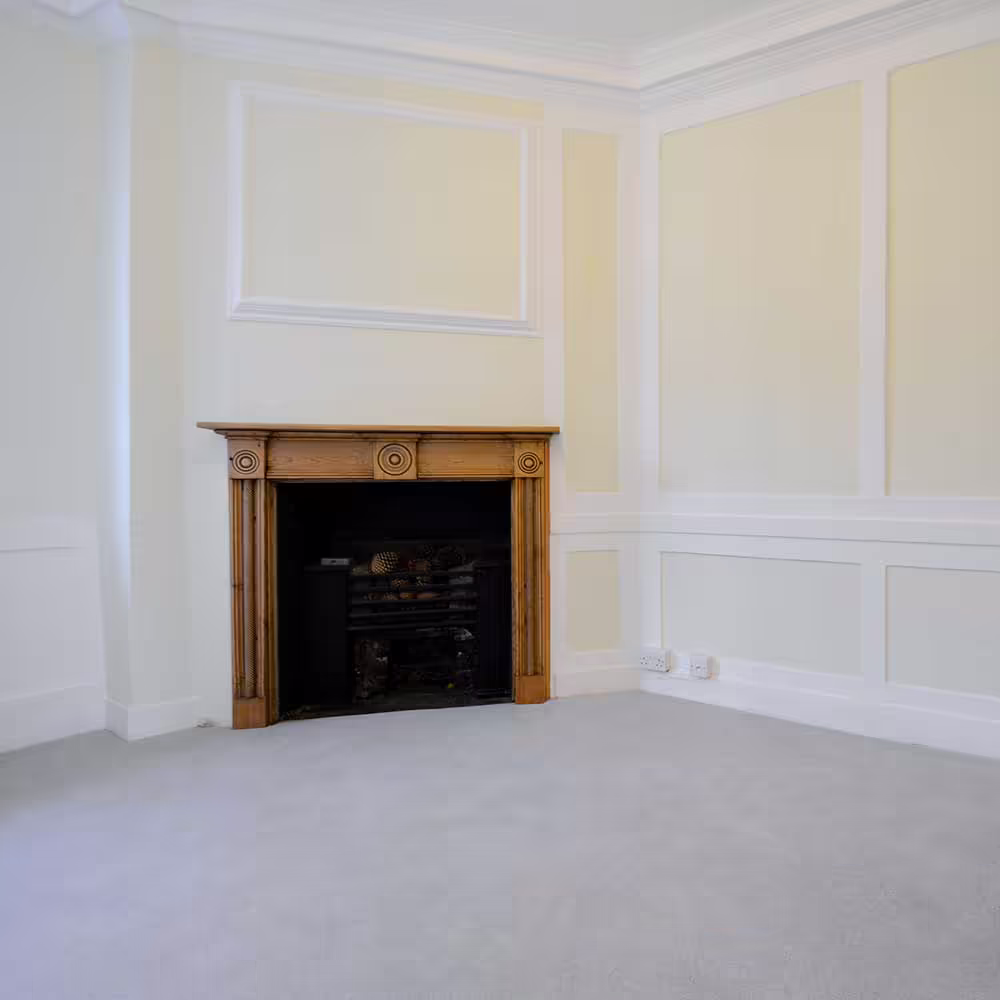 A corner of a refurbished room featuring detailed wall panelling, a dark wooden Victorian-style fire surround, and new light grey carpeting, illustrating the interior restoration of the void property.