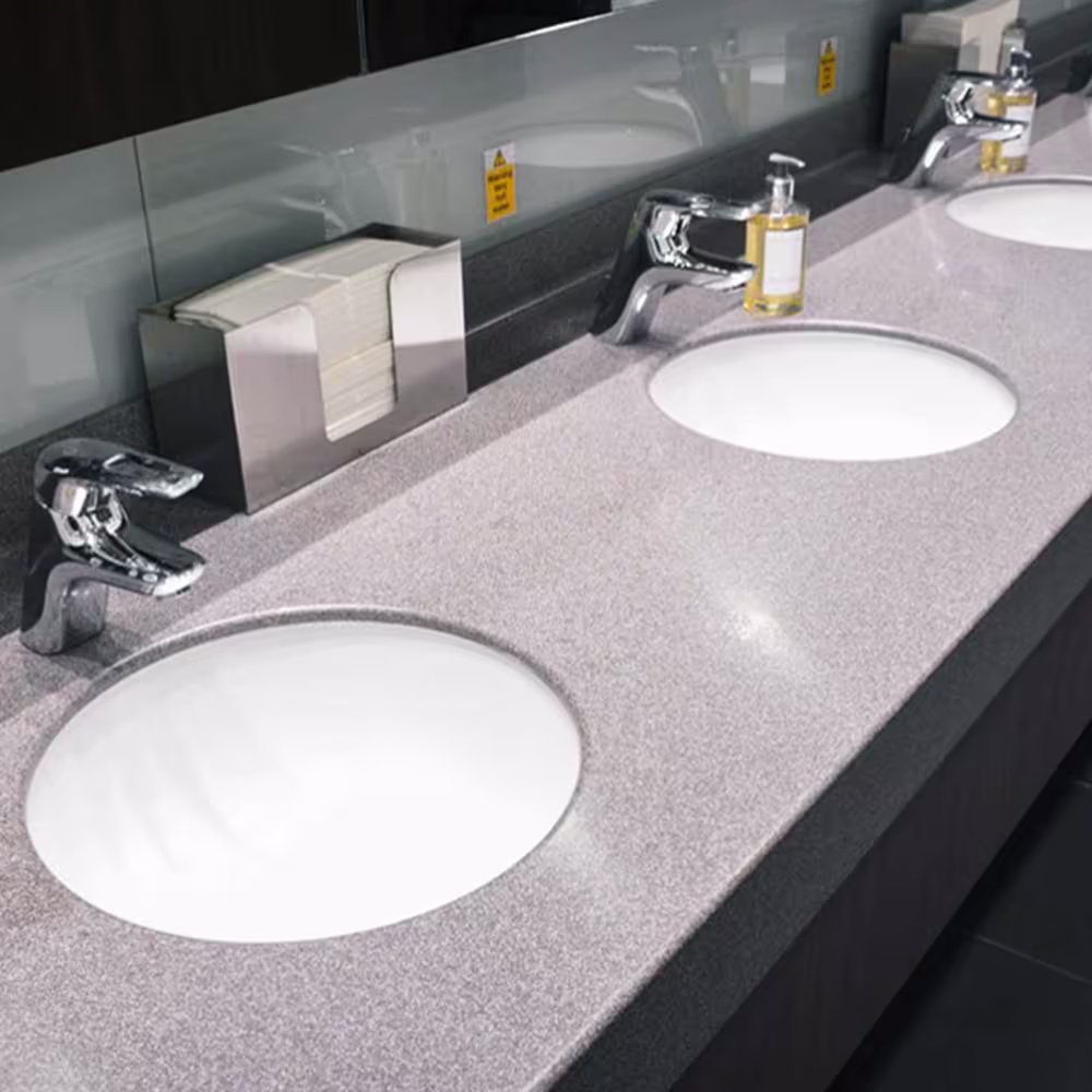 A close-up of a newly installed commercial washroom vanity unit, featuring a light grey speckled countertop with multiple white inset sinks, modern chrome taps, and a mirror/splashback area, showcasing the washroom refurbishment quality.