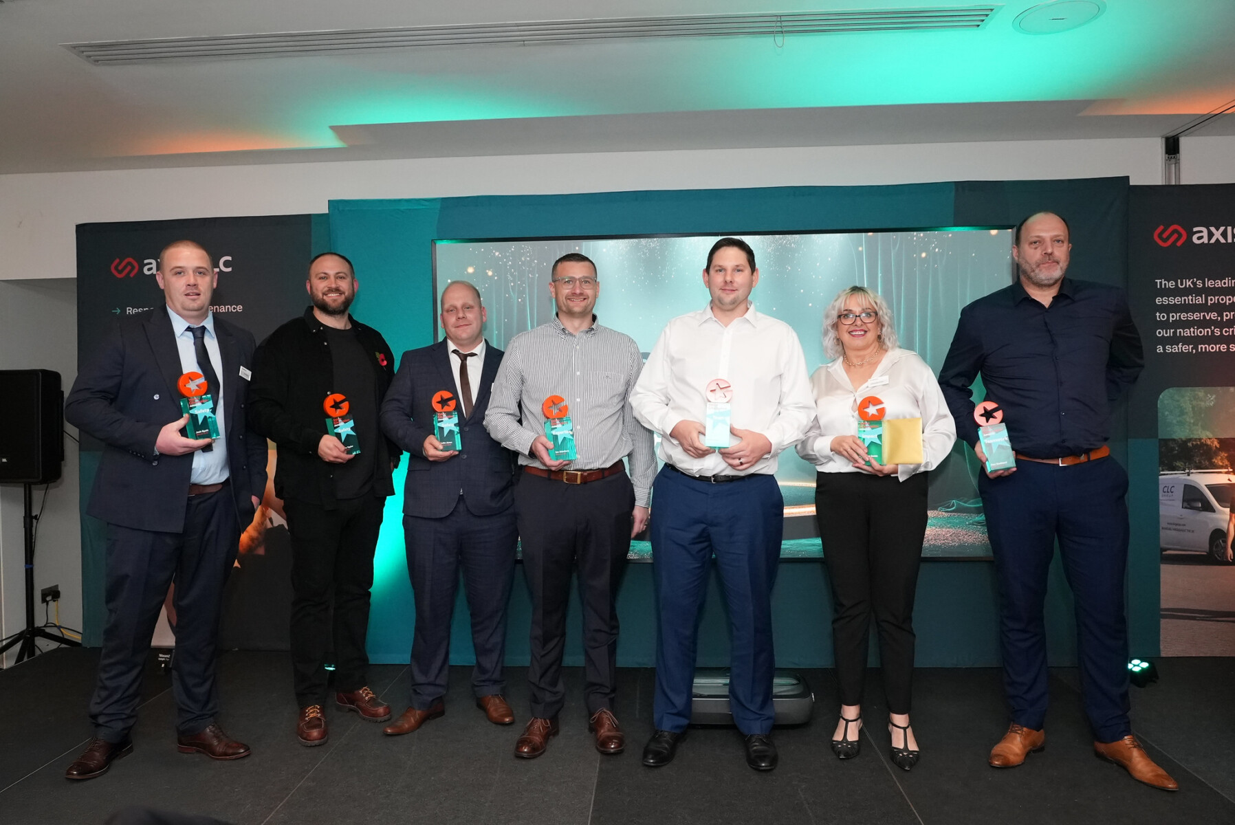Group of men and one woman holding trophies smiling at the camera