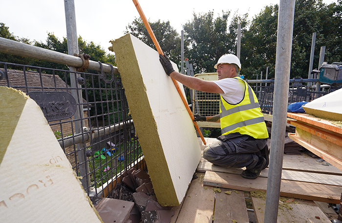 operative in high vis and a white hard hat measuring and cutting insulation on scaffolding