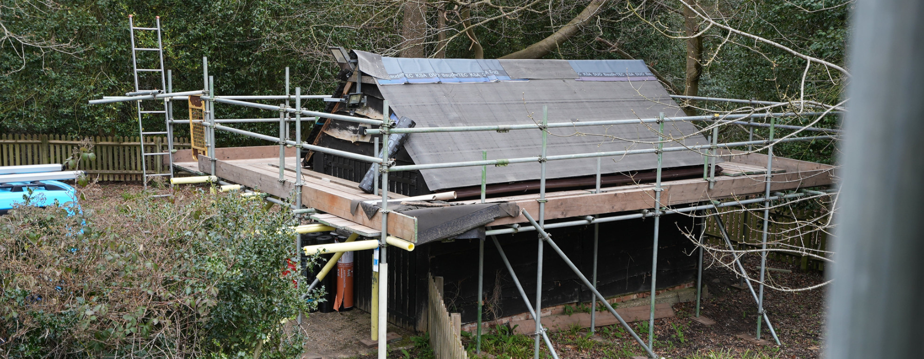 Exterior of a wooden large lodge with scaffolding around it. Outside in a green garden