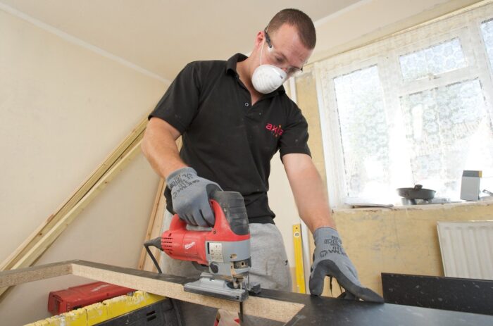 carpenter cutting into kitchen counter with jigsaw in residential void property