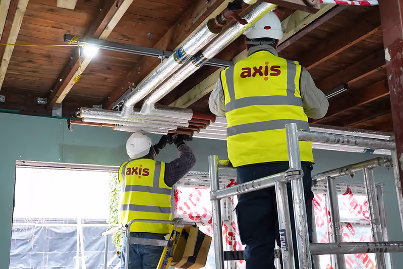Two Axis employees in high-vis vests working together on top of a scaffold tower.