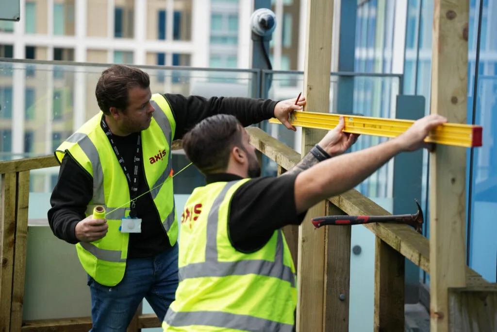 Two Axis employees working together to measure and markup exterior wood on a building, representing learning more about Axis.