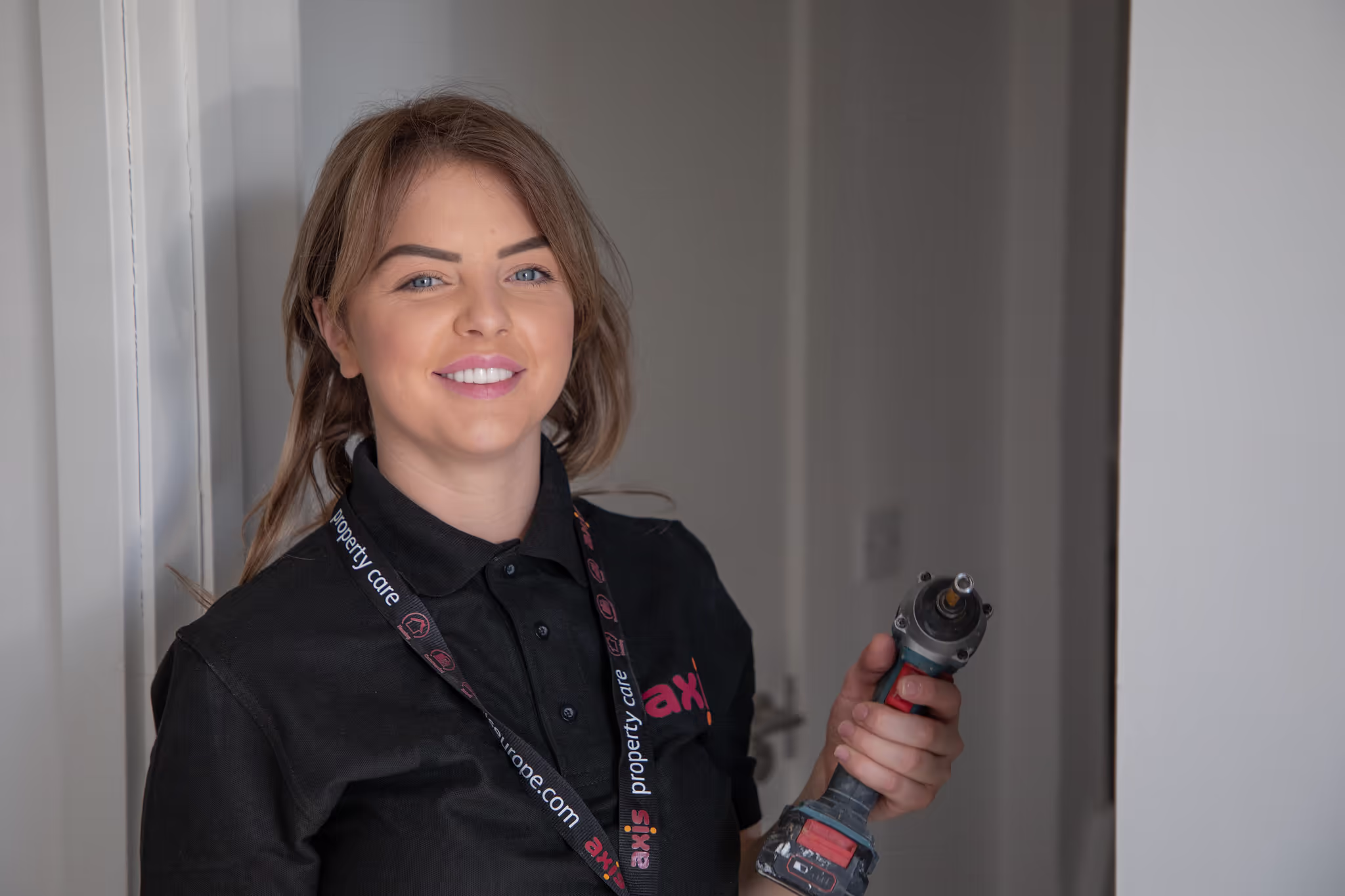 A friendly female Axis property care operative smiles at the camera while holding a power drill, ready for a maintenance job.