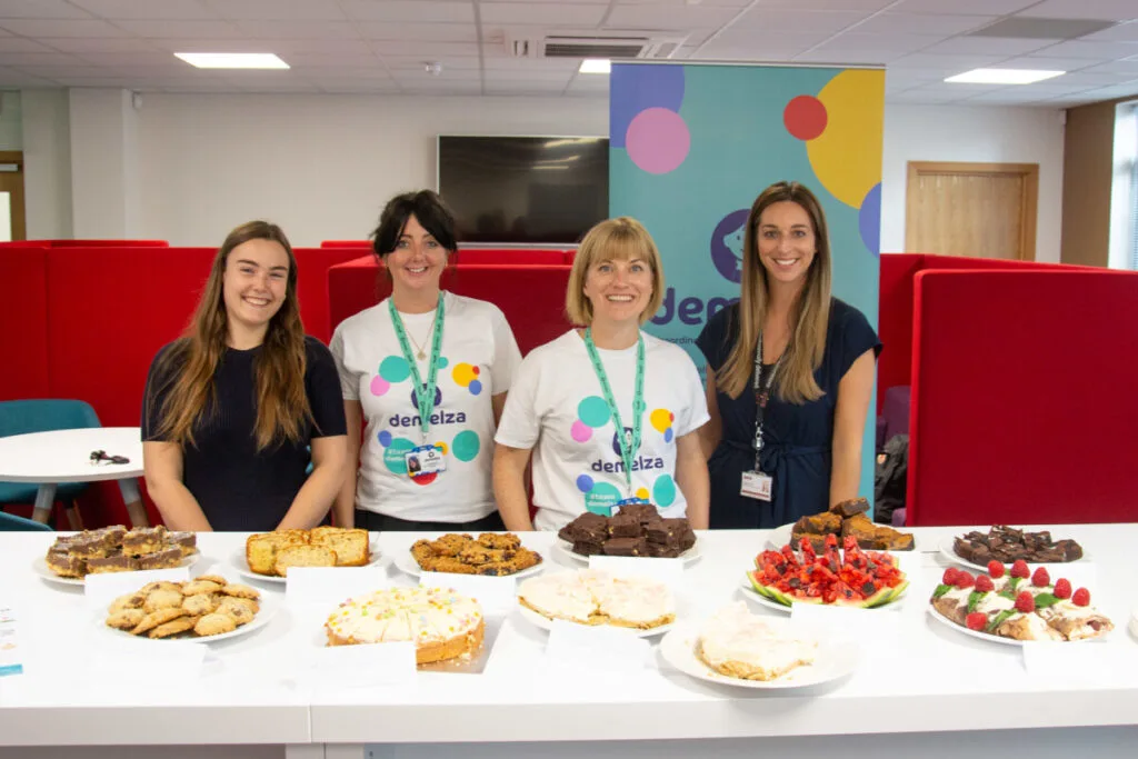 Four Axis employees smiling next to a bake sale.