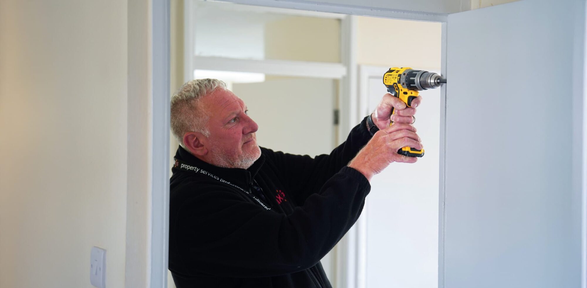 An Axis handyman provides responsive repairs, carefully using a power drill on a white interior door frame.