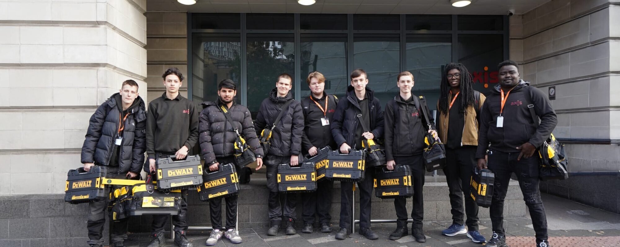 A group of varied trade apprentices outside a building holding dewalt tool boxes.